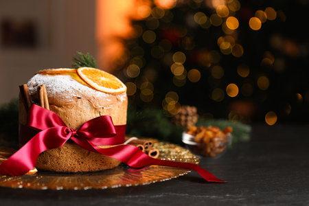 Christmas food. Delicious Panettone cake, ingredients and festive decor on black table against background with blurred lights, space for text. Bokeh effectの写真素材