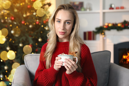 Beautiful woman with tasty hot cocoa in room decorated for Christmasの写真素材
