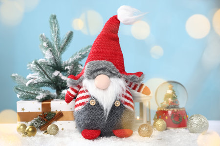 Funny Christmas gnome and festive decor on artificial snow against light blue background with...