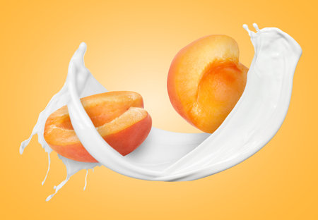 Milkshake splash and apricot halves in air on orange backgroundの写真素材