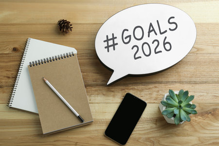 New 2026 Year Goals. Notebooks, paper speech bubble and mobile phone on wooden table, top view