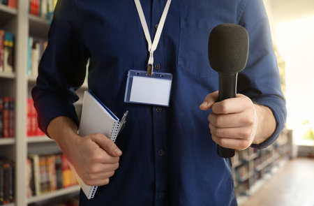 Journalist with microphone and notebook near shelves in library, closeupの写真素材