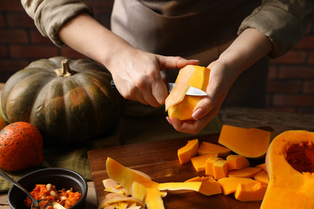 Woman peeling pumpkin at wooden table against brick wall, closeupの写真素材