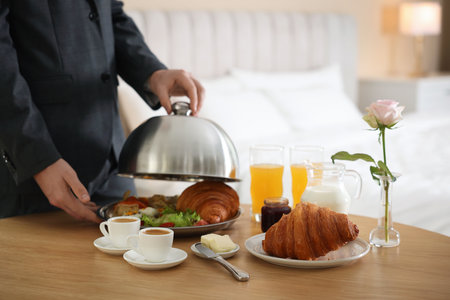 Waiter serving breakfast on wooden table in hotel room, closeup. Space for textの写真素材