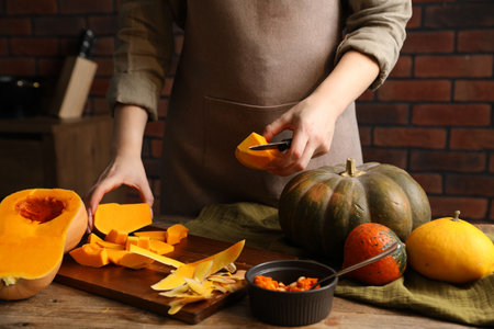 Woman cutting pumpkin at wooden table against brick wall, closeupの写真素材