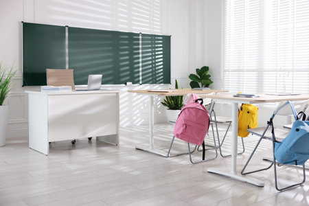 Green chalkboard, desks and chairs with backpacks in classroom