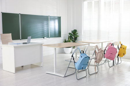 Green chalkboard, backpacks and stylish furniture in classroom. Mockup for designの写真素材
