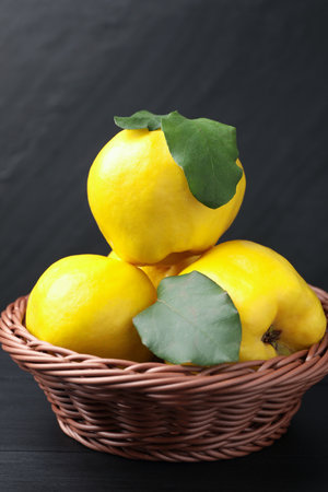 Ripe quinces with green leaves in wicker basket on black wooden table, closeupの写真素材