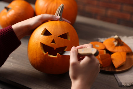 Woman carving pumpkin for Halloween at wooden table, closeupの写真素材