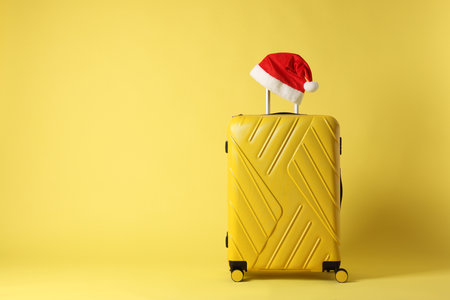 Stylish suitcase with Santa hat on yellow background, space for text. Christmas vacationの写真素材