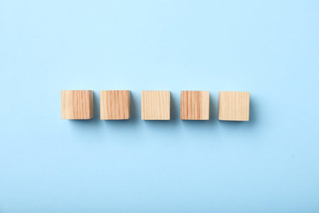Wooden cubes on light blue background, top view