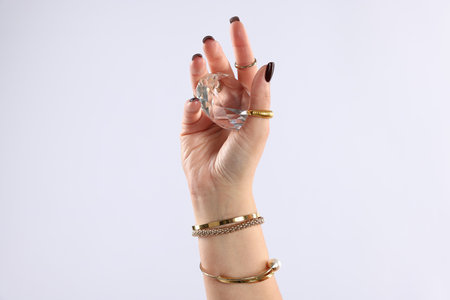 Young woman wearing stylish gold rings and holding diamond on light gray background, closeupの写真素材