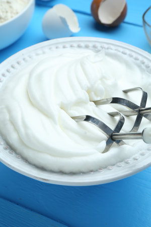 Whipped egg whites in bowl, mixer and products on blue wooden table, closeupの写真素材