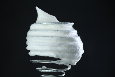 Whisk with whipped egg whites on black backgroundの写真素材