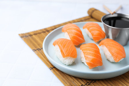 Delicious nigiri sushi with salmon and soy sauce on light tiled table, closeup. Space for textの写真素材