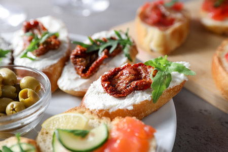 Tasty bruschettas with salmon, cucumber, cream cheese, sun dried tomatoes and olives on gray textured table, closeupの写真素材