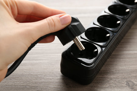 Woman putting plug into power strip at wooden table, closeup
