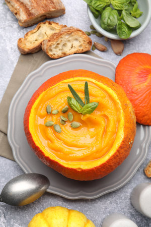 Tasty pumpkin cream soup with seeds and basil served in pumpkin on gray table, flat layの写真素材
