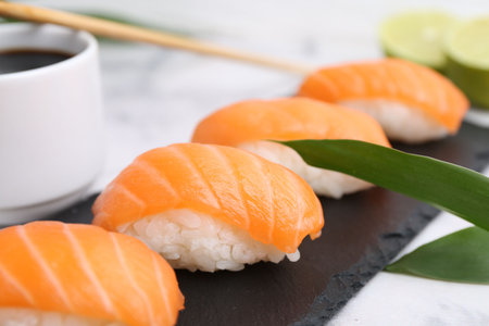 Delicious nigiri sushi with salmon, soy sauce and green leaves on light table, closeupの写真素材