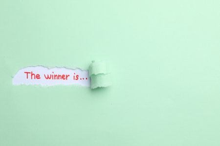 Phrase The Winner Is on white background, view through hole in torn pale green paper. Space for textの写真素材