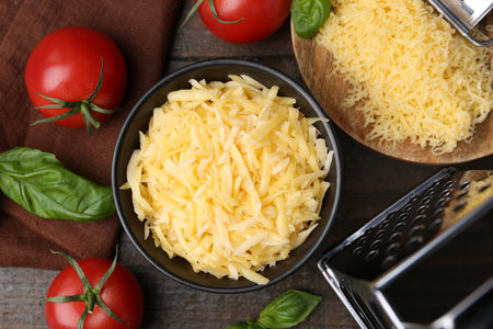 Grated cheese, grater, tomatoes and basil on wooden table, flat layの写真素材