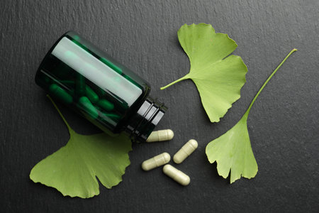 Ginkgo biloba leaves and medical bottle with pills on dark textured table, flat layの写真素材