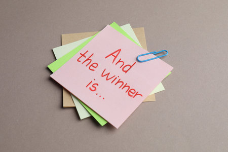 Sticky notes with phrase And The Winner Is on gray background, closeupの写真素材