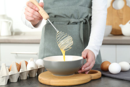 Woman beating eggs at gray table in kitchen, closeup