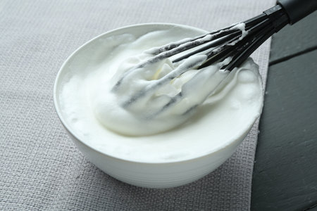 Whipped whites in bowl on gray wooden table, closeup