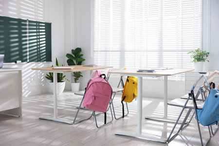 Green board, desks and chairs with backpacks in classroom