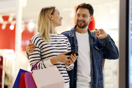 Happy couple with shopping bags and smartphone in mall