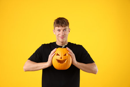 Halloween celebration. Man holding pumpkin with carved face on yellow backgroundの写真素材