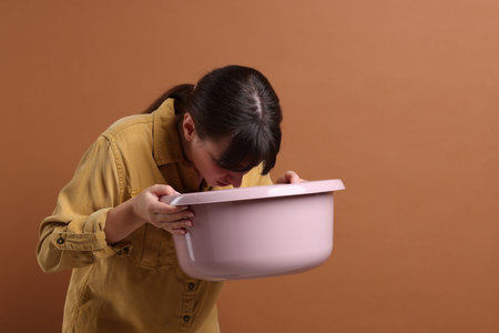 Young woman with basin suffering from nausea on brown background, space for textの写真素材