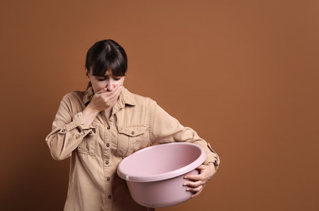 Young woman with basin suffering from nausea on brown background, space for textの写真素材