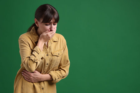 Young woman suffering from stomachache and nausea on green background, space for textの写真素材