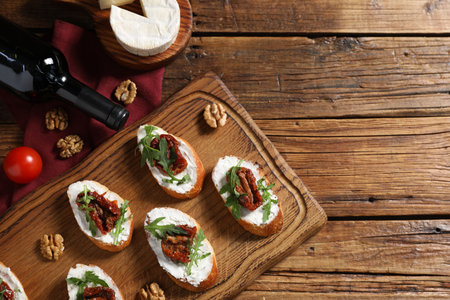 Delicious bruschettas with cream cheese, sun-dried tomatoes, arugula on wooden table, flat lay. Space for textの写真素材