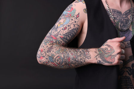 Young man with tattoos and stylish clothes posing on dark gray background, closeup. Space for text