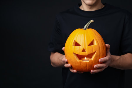 Halloween celebration. Man with jack o'lantern pumpkin on black background, closeup. Space for textの写真素材