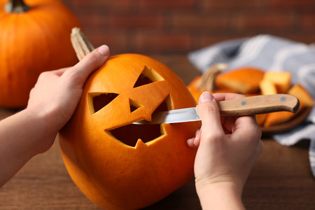Woman carving pumpkin for Halloween at wooden table, closeupの写真素材