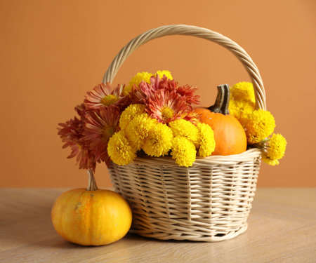 Beautiful autumn composition with flowers and pumpkins on wooden table against orange backgroundの写真素材