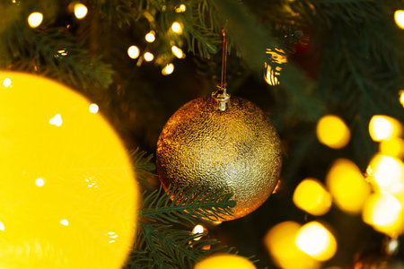 Christmas bauble hanging on fir tree branch against blurred festive lights, closeup. Bokeh effectの写真素材