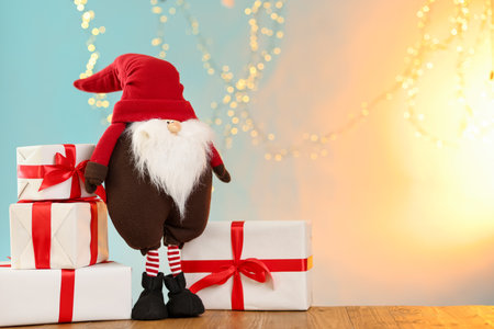 Christmas gnome and gift boxes on wooden table against color gradient background with blurred lights, space for text. Bokeh effectの写真素材