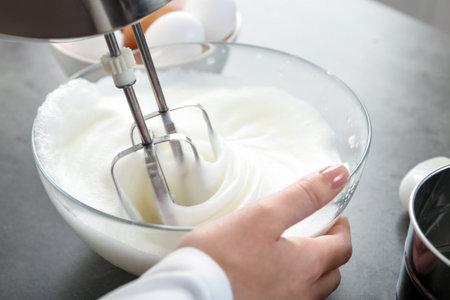 Woman beating egg whites with mixer at gray table, closeupの写真素材