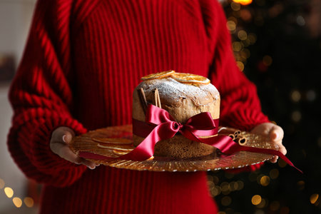 Christmas food. Woman with delicious Panettone cake against background with blurred lights, closeup. Bokeh effectの写真素材