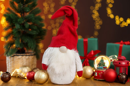 Christmas gnome, gift boxes and festive decor on wooden table against dark orange background with blurred lights, closeup. Bokeh effectの写真素材