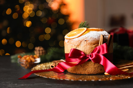 Christmas food. Delicious Panettone cake, ingredients and festive decor on black table against background with blurred lights, space for text. Bokeh effectの写真素材