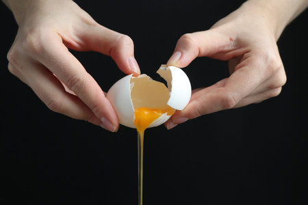 Woman cracking egg on black background, closeup