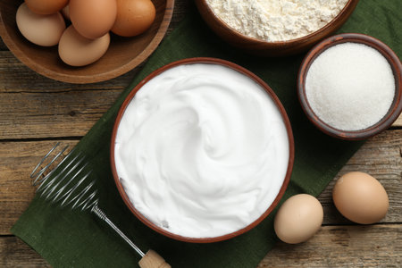 Whipped egg whites in bowl, ingredients on wooden table, flat layの写真素材