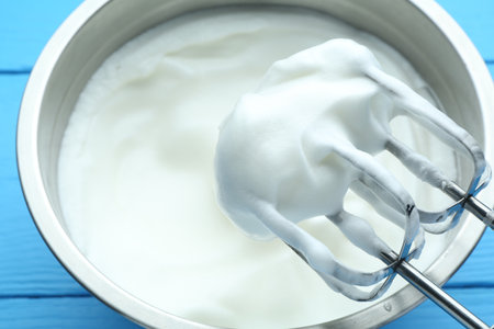Whipped egg whites in bowl and mixer on blue wooden table, closeupの写真素材