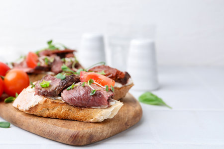 Delicious bruschettas with roast beef served on white tiled table, closeup. Space for textの写真素材